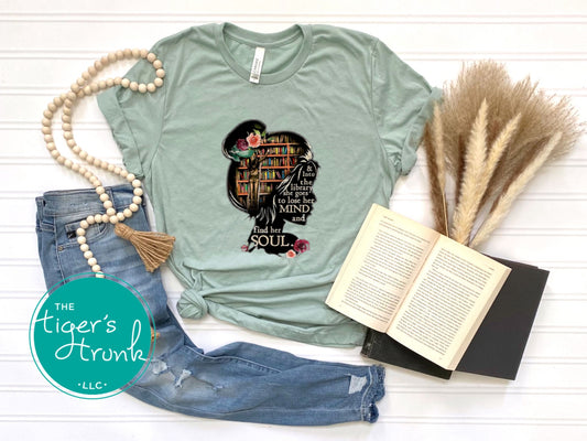 Mint green t-shirt with a graphic design, paired with jeans and an open book on a white surface, branded 'The Tiger's Trunk'.