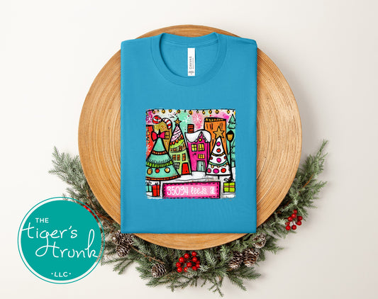 Aqua Christmas shirt featuring a colorful whimsical holiday village and the zip code 35094 Leeds AL.