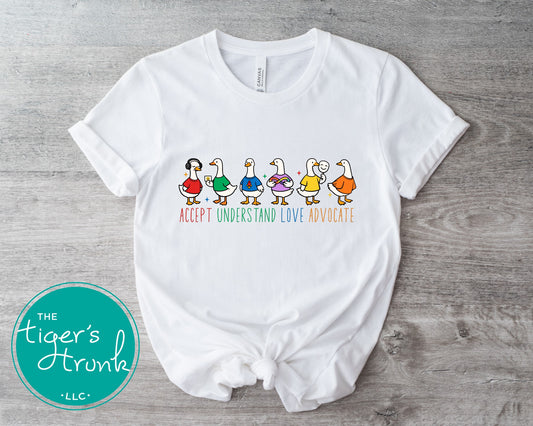 White t-shirt with colorful duck illustrations and text on a wooden surface, branded 'The Tiger's Trunk'.