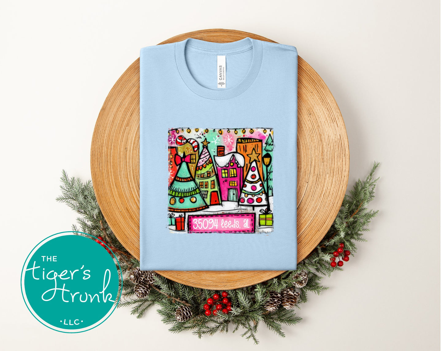 Baby blue Christmas shirt with a bright colorful holiday village and the 35094 Leeds AL zip code.