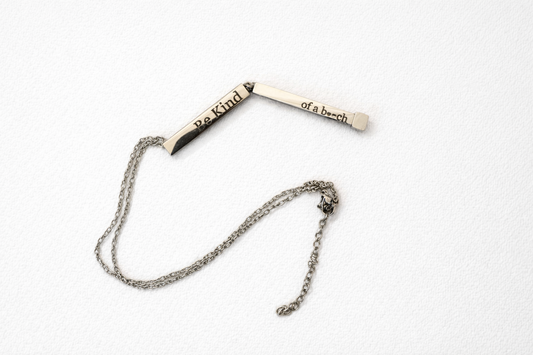 Engraved bar necklace opened to reveal the phrase Be Kind of a Bitch on a minimalist silver bar pendant with chain.