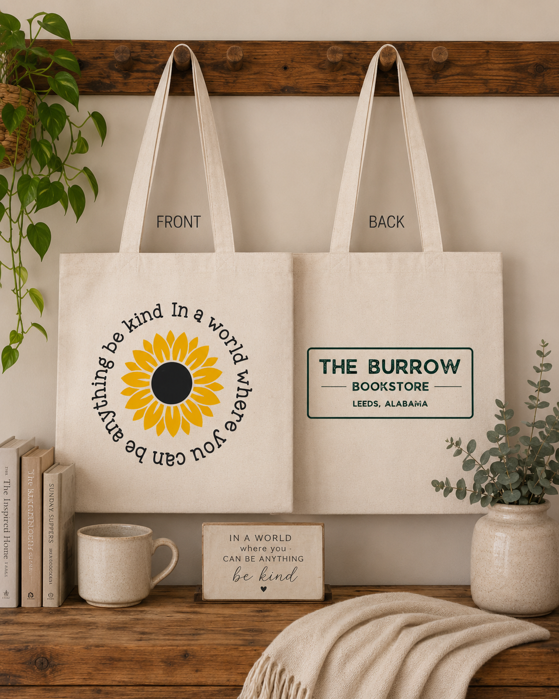 Natural canvas two-sided tote bag featuring a sunflower with the phrase Be Kind in a World Where You Can Be Anything on the front and The Burrow Bookstore logo on the back.