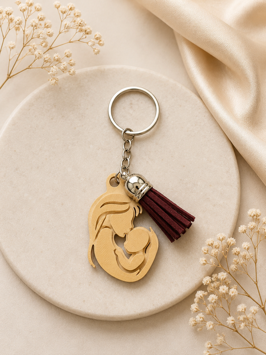 Beige mother and baby silhouette keychain with burgundy tassel displayed on an elegant neutral flat lay background with delicate floral accents and satin fabric