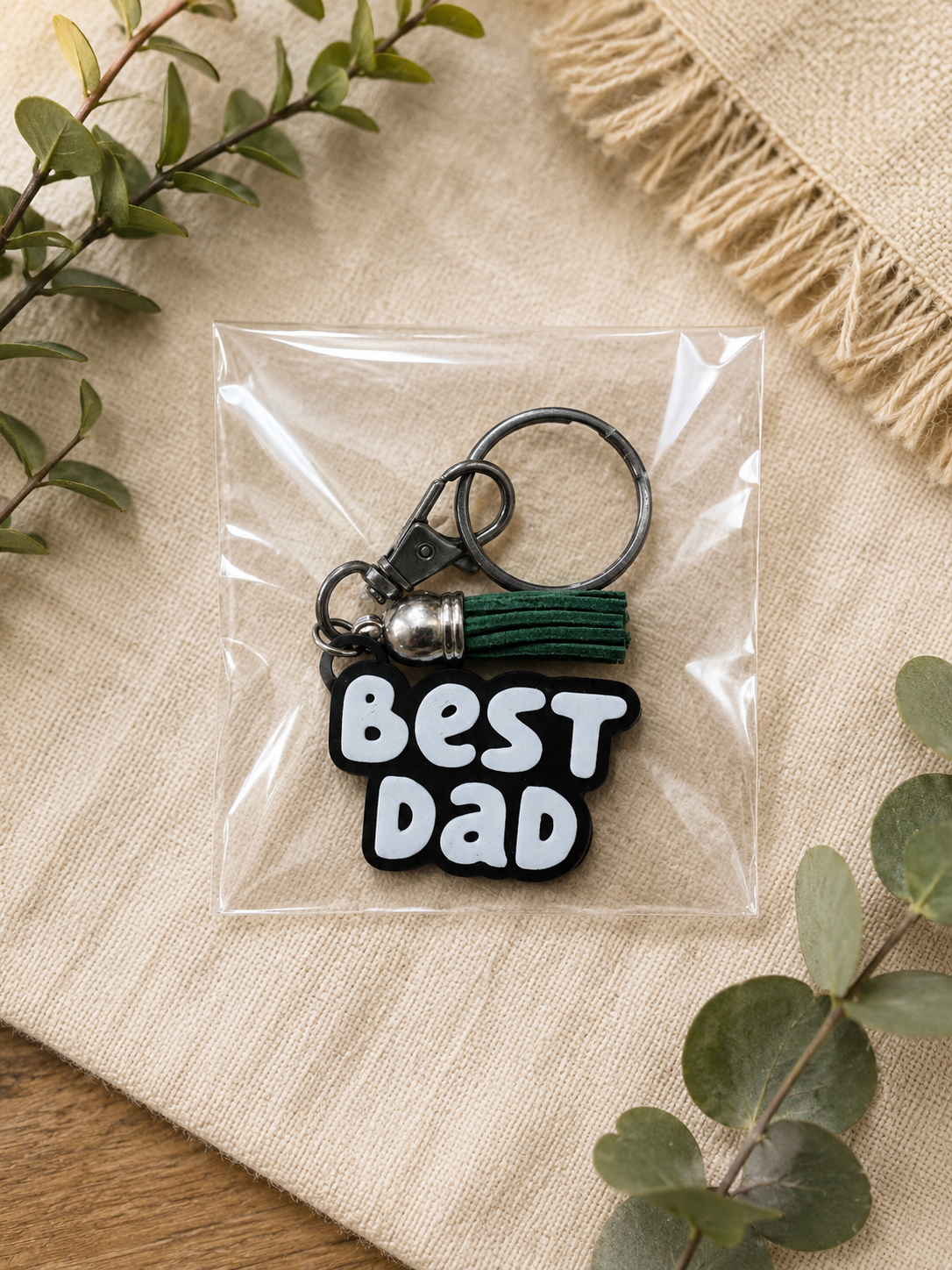 Black and white Best Dad keychain with green tassel packaged in clear gift bag