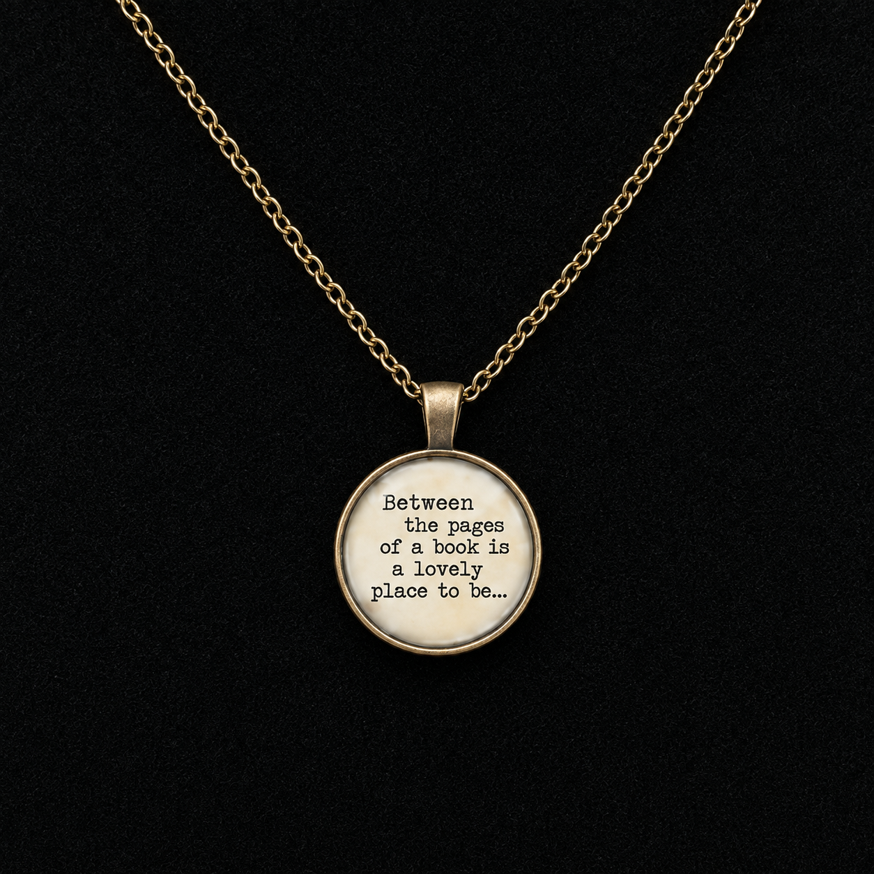 A gold chain necklace with a round pendant featuring the quote 'Between the pages of a book is a lovely place to be.