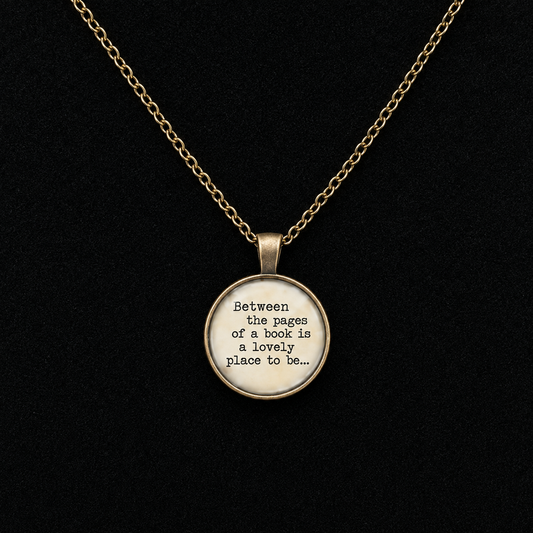 A gold chain necklace with a round pendant featuring the quote 'Between the pages of a book is a lovely place to be.