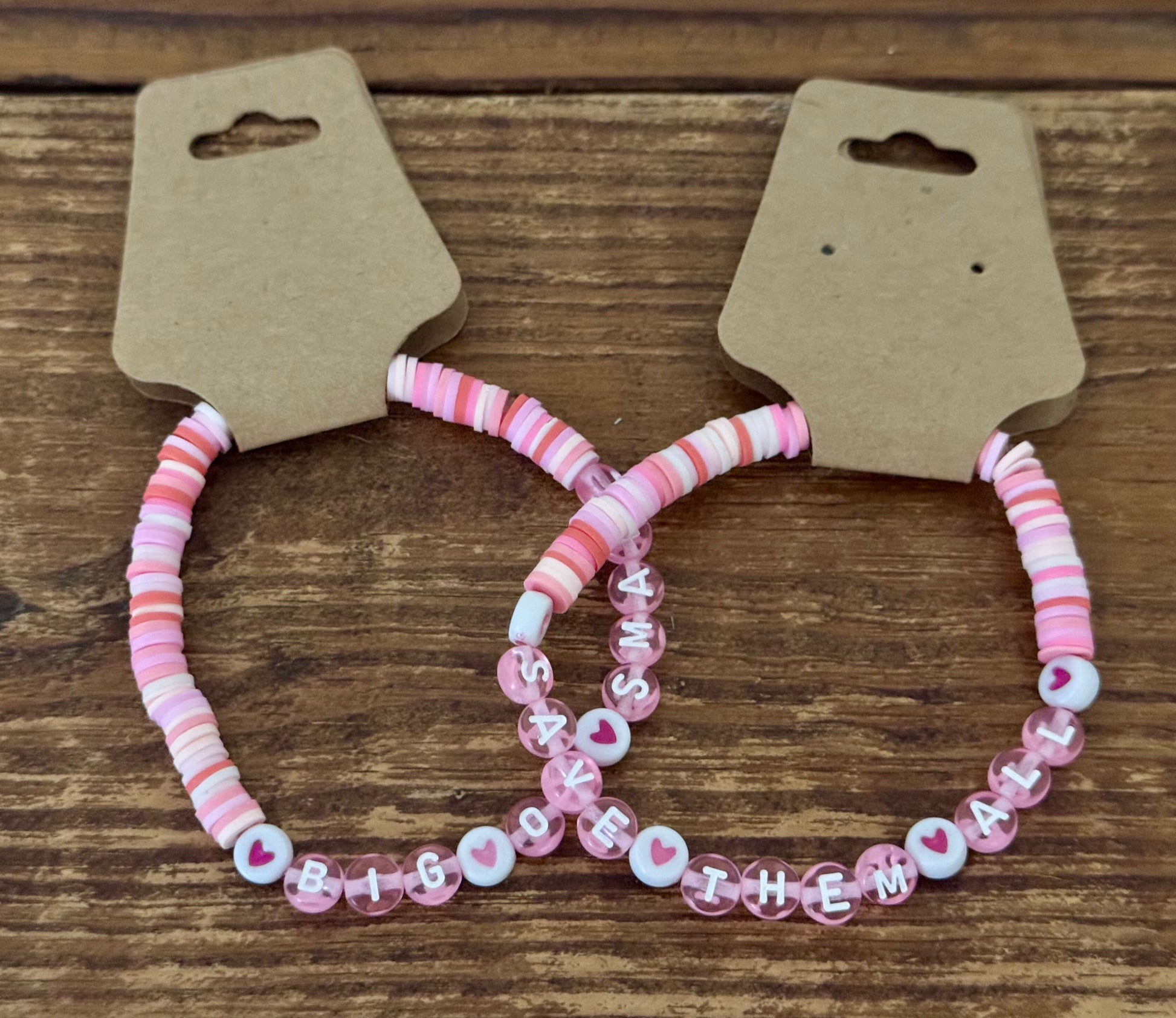 Two pink beaded bracelets on a wooden surface with cardboard holders.
