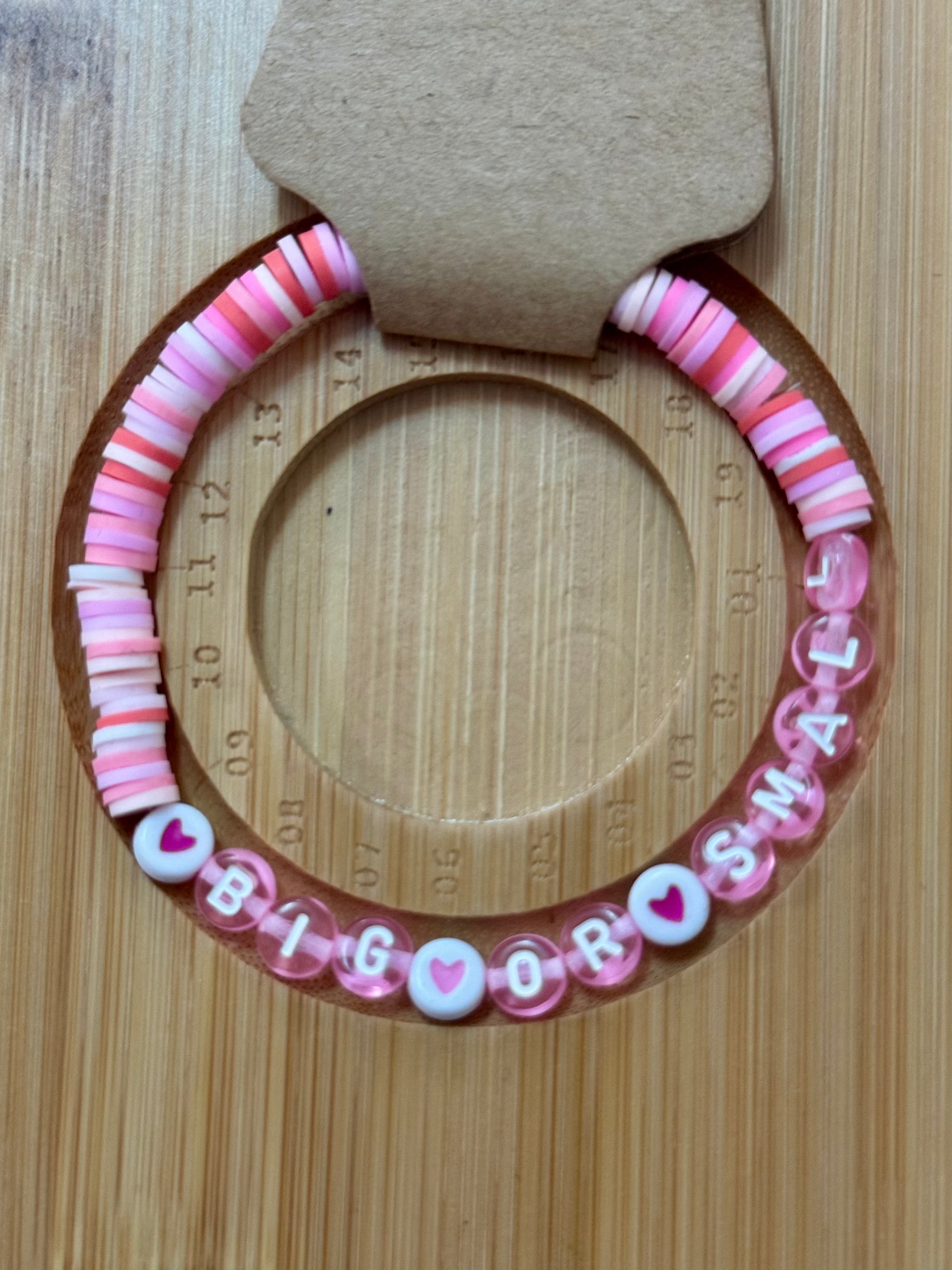 Pink and white beaded bracelet with 'BIG BROTHER' text on a wooden surface