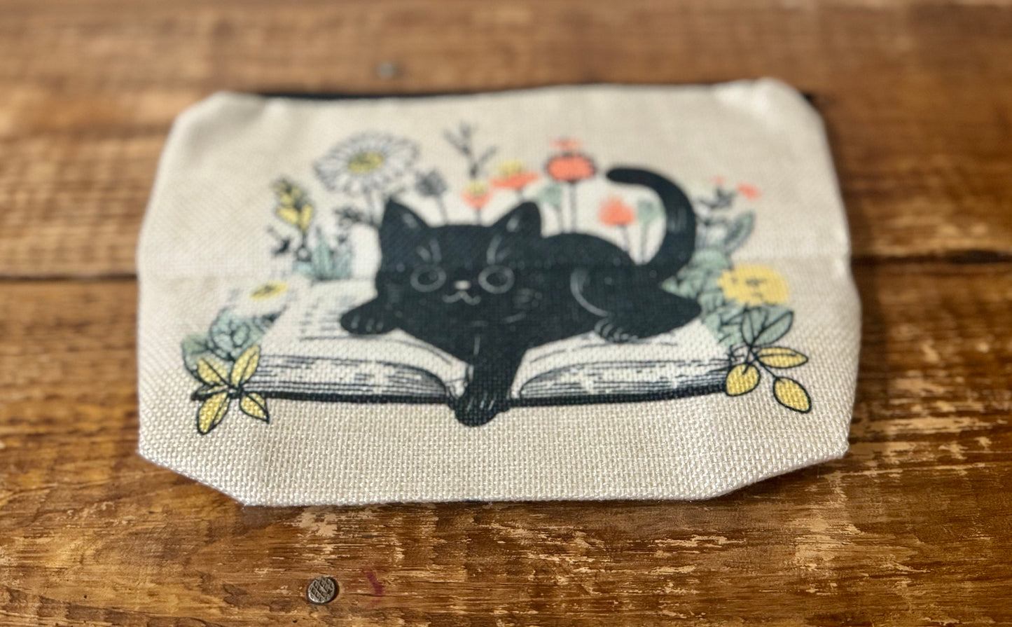 A 6.5"x8.5" accessories pouch featuring an illustration of a black cat lounging on a stack of books, perfect for book lovers and cat enthusiasts.