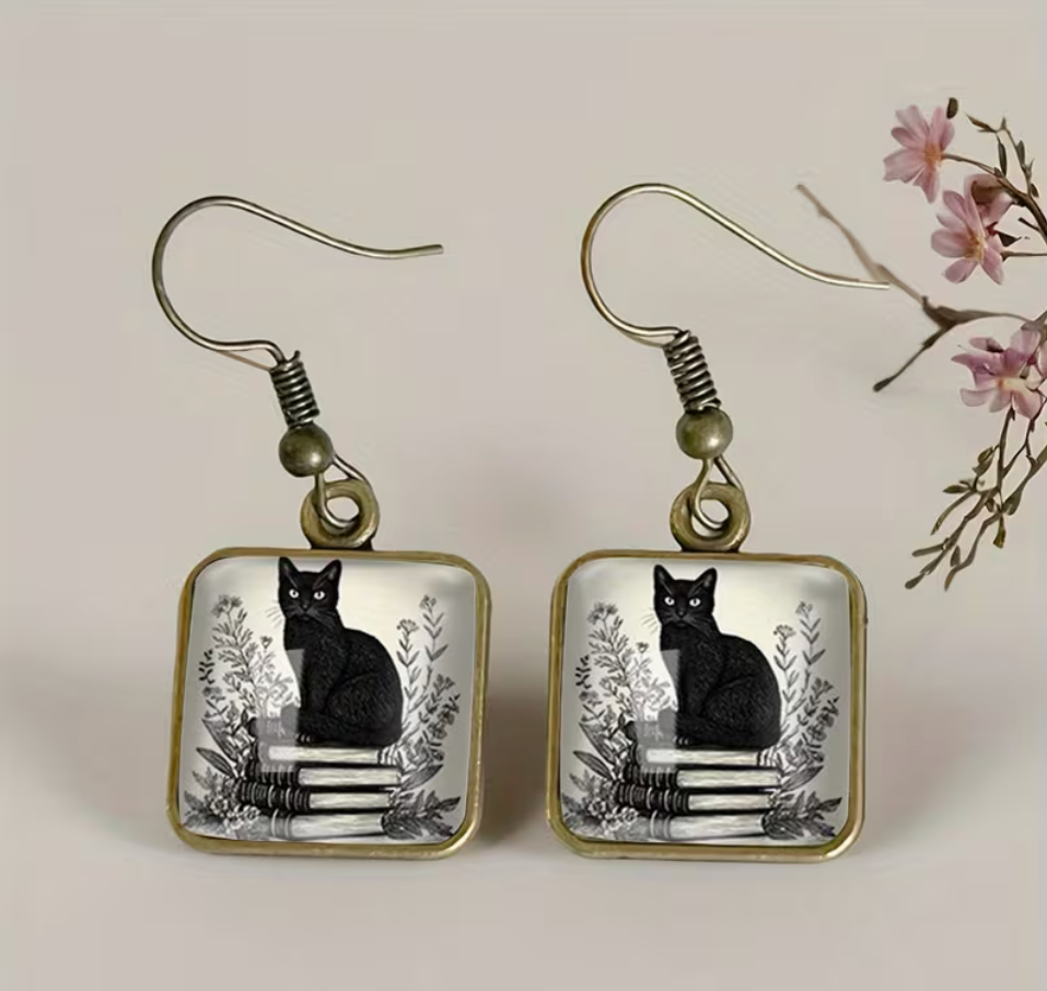 lack cat sitting on stacked books square glass dangle earrings with antique gold-tone frames