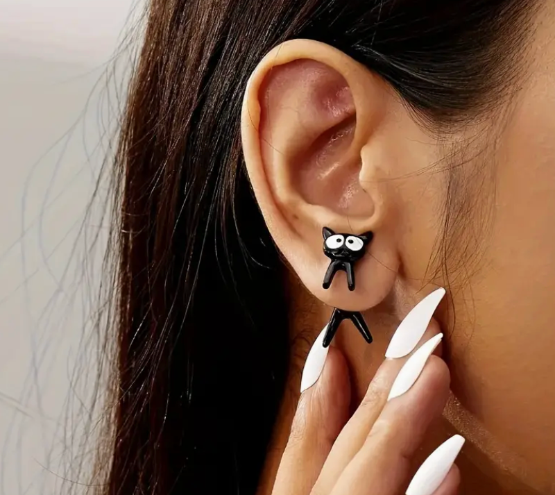 Black cat-shaped earring worn by a person with white nail polish.
