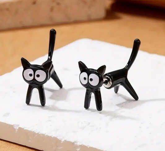 Black cat-shaped earrings on a white surface with a wooden background