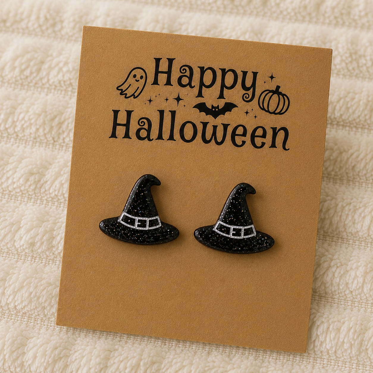 Black glitter witch hat stud earrings with silver buckle detail displayed on a Halloween earring card.