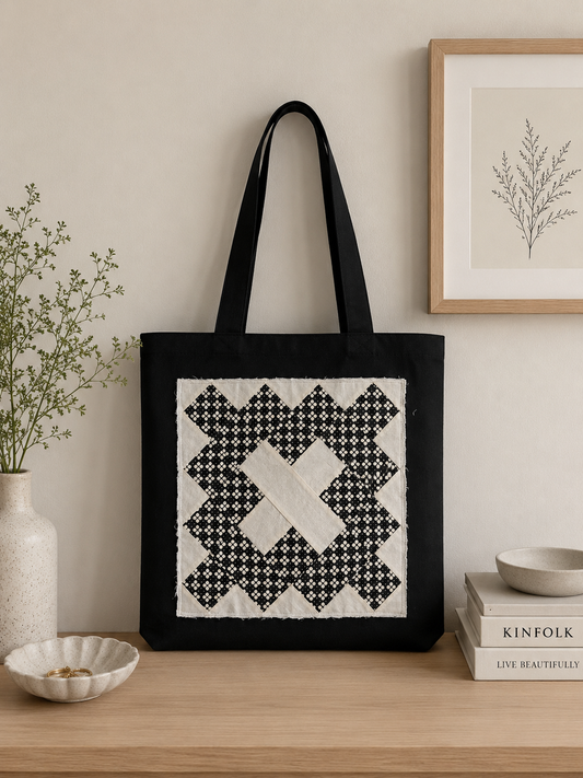 Black canvas tote bag featuring handmade black and cream quilt-inspired patchwork panel