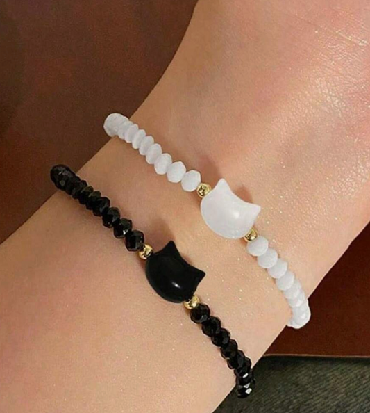Two bracelets on a wrist, one black with cat-shaped beads and the other white with similar design.