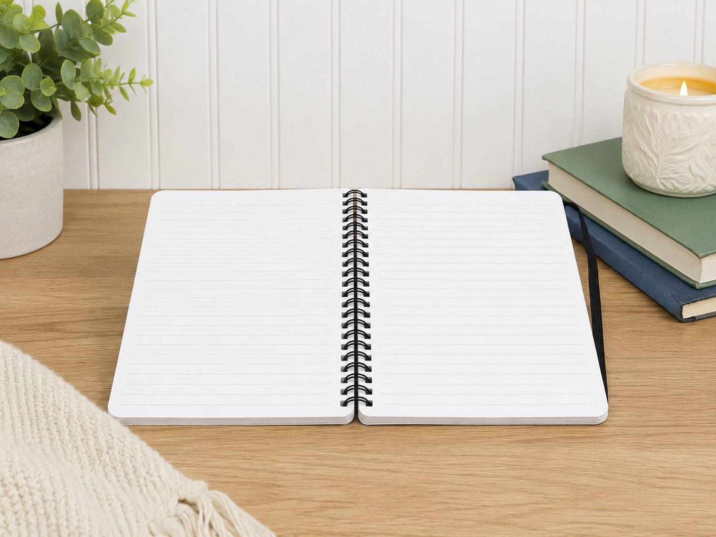 Open notebook on a wooden surface with a plant and books in the background