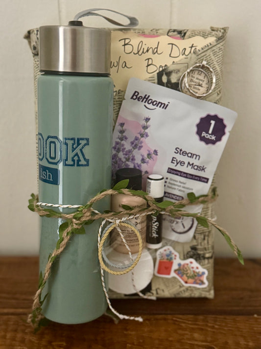 Gift basket with a water bottle, eye mask, and other items on a wooden surface.