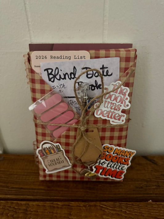 Front view of Blind Date with a Book historical fiction gift wrapped in red gingham paper, tied with twine, featuring stickers, pen, reading list card, and bookmark, displayed on wooden surface.