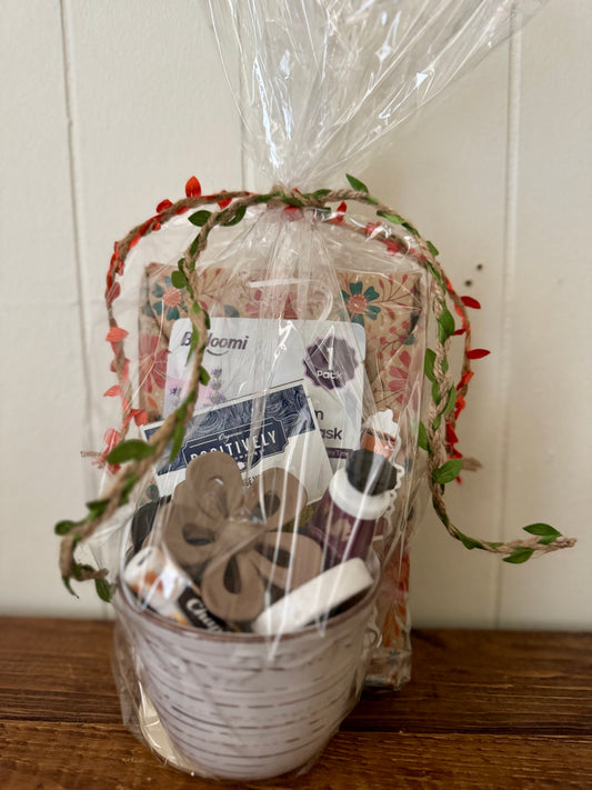 Gift basket with items including a roll of paper towels, a bottle of hand sanitizer, and a box of tissues, wrapped in cellophane with decorative ribbons.