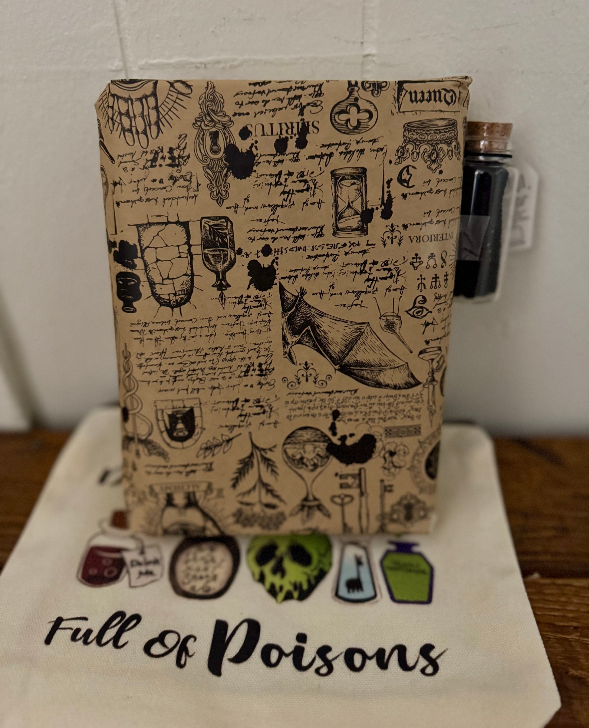 Notebook with vintage-style poison bottle and skull design on a white surface with 'Full of Poisons' text.