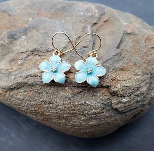 Light blue cherry blossom flower drop earrings with gold hooks displayed on stone background