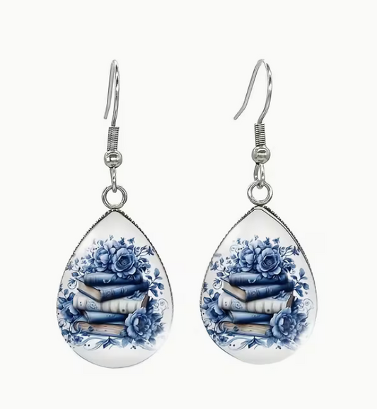 Teardrop dangle earrings featuring blue floral artwork surrounding a stack of books in a silver-tone setting.