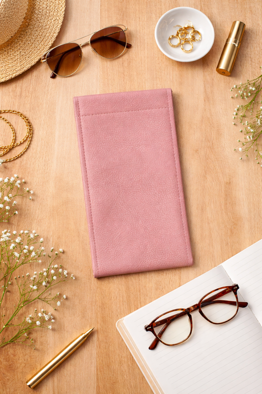 Blush pink slim faux leather reading and sunglasses holder displayed in a styled flat lay with sunglasses, notebook, pen, and gold accessories.