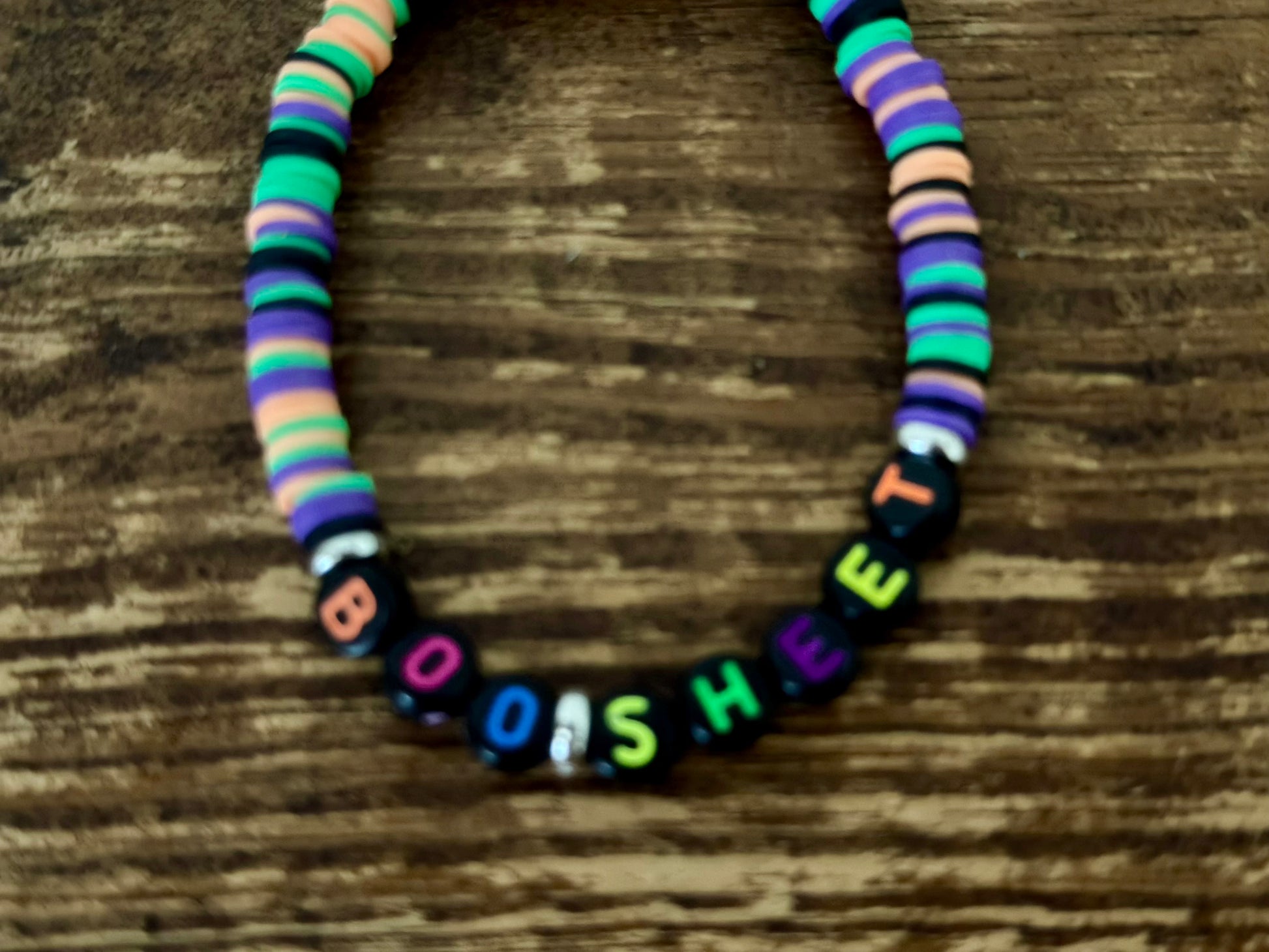Colorful beaded necklace with multicolored beads and black beads with colorful letters on a wooden surface.