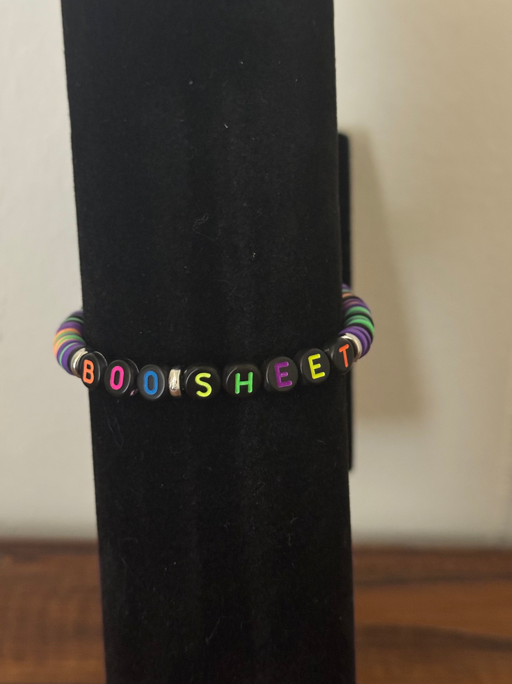 Colorful beaded bracelet with letters spelling 'BOOISHEAT' on a black stand.