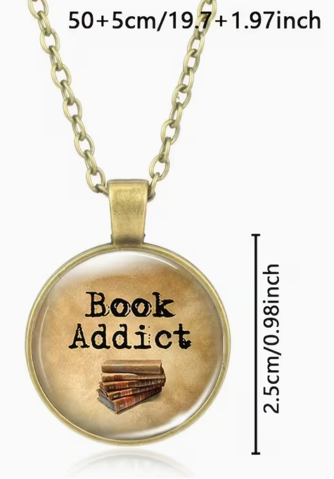 A round pendant necklace with a vintage-style gold-toned frame and chain, featuring the words 'Book Addict' and an illustration of stacked books on a parchment-like background. Measurement text and a vertical dimension marker are overlaid on the image.