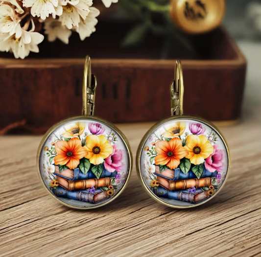 Round antique bronze dangle earrings featuring colorful flowers arranged on stacked books beneath a glossy glass cabochon.