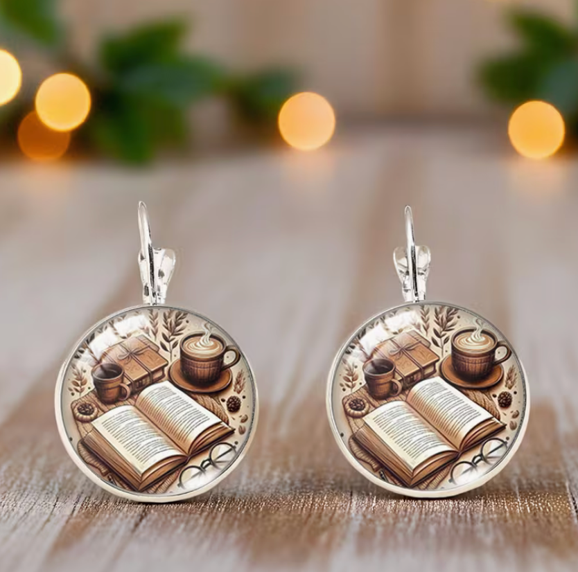 Round glass cabochon dangle earrings featuring an open book, coffee cup, and cozy reading scene in a silver-tone setting.