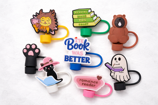 Assorted book-themed silicone straw toppers including lion with tea, reading stack, bear, ghost with book, black cat reading, romance reader, paw print, and The Book Was Better design.
