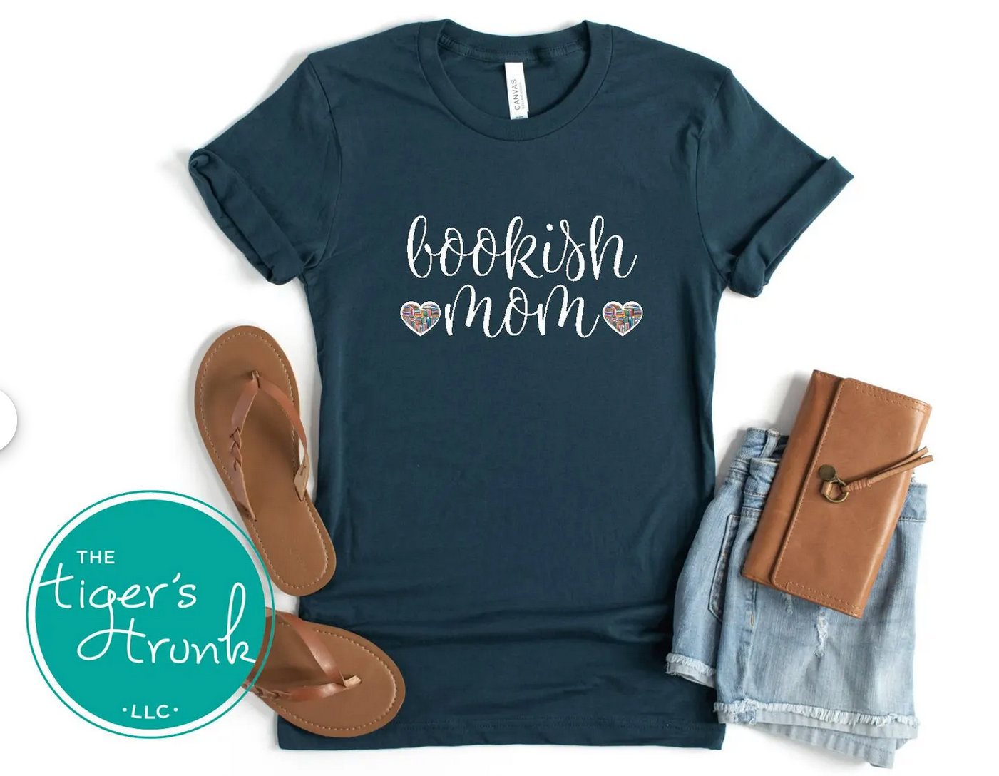 Navy blue t-shirt with 'bookish mom' text, sandals, denim shorts, and a notebook on a white background.