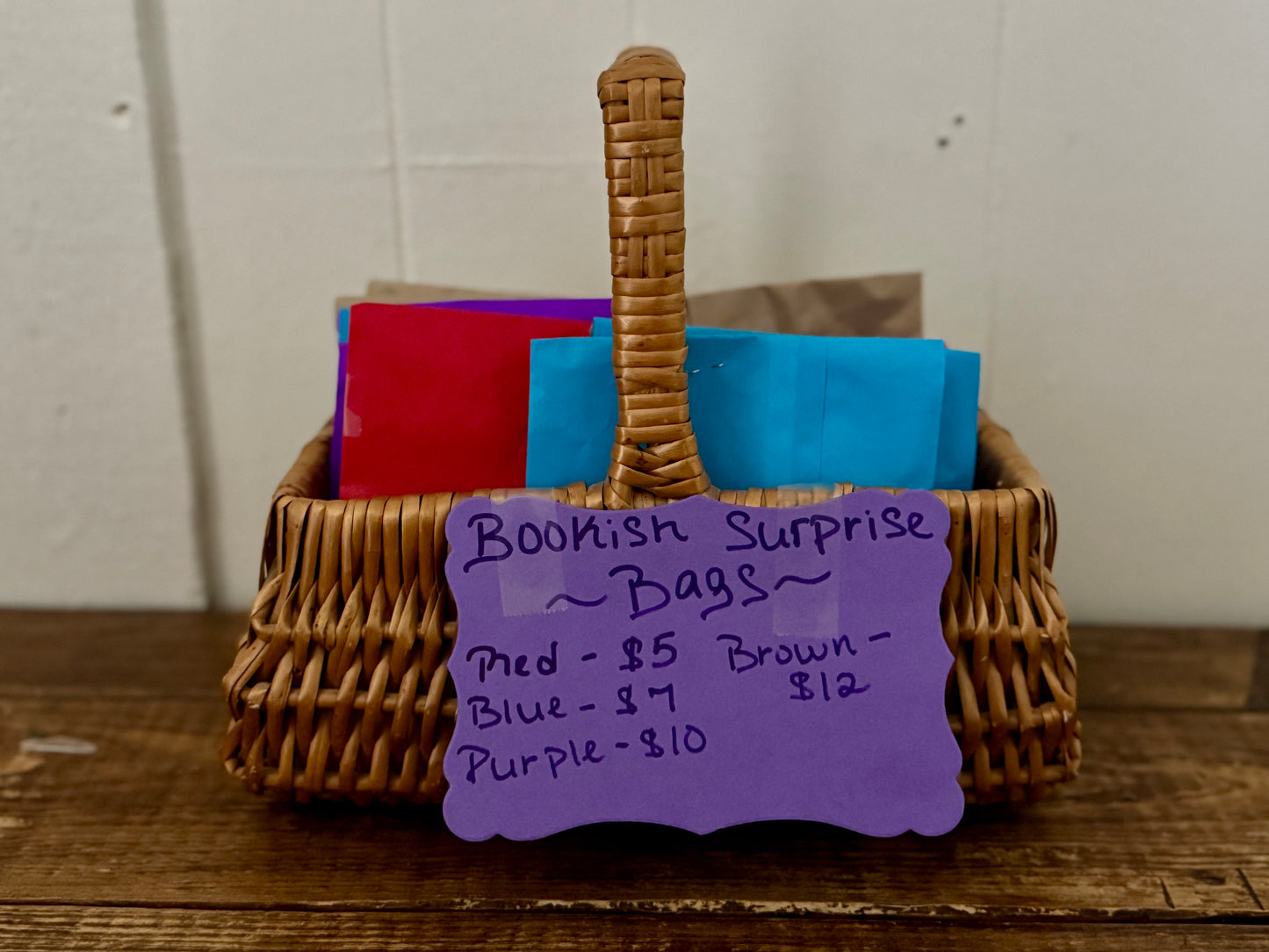 Wicker basket with colorful bags and a purple sign on a wooden surface.