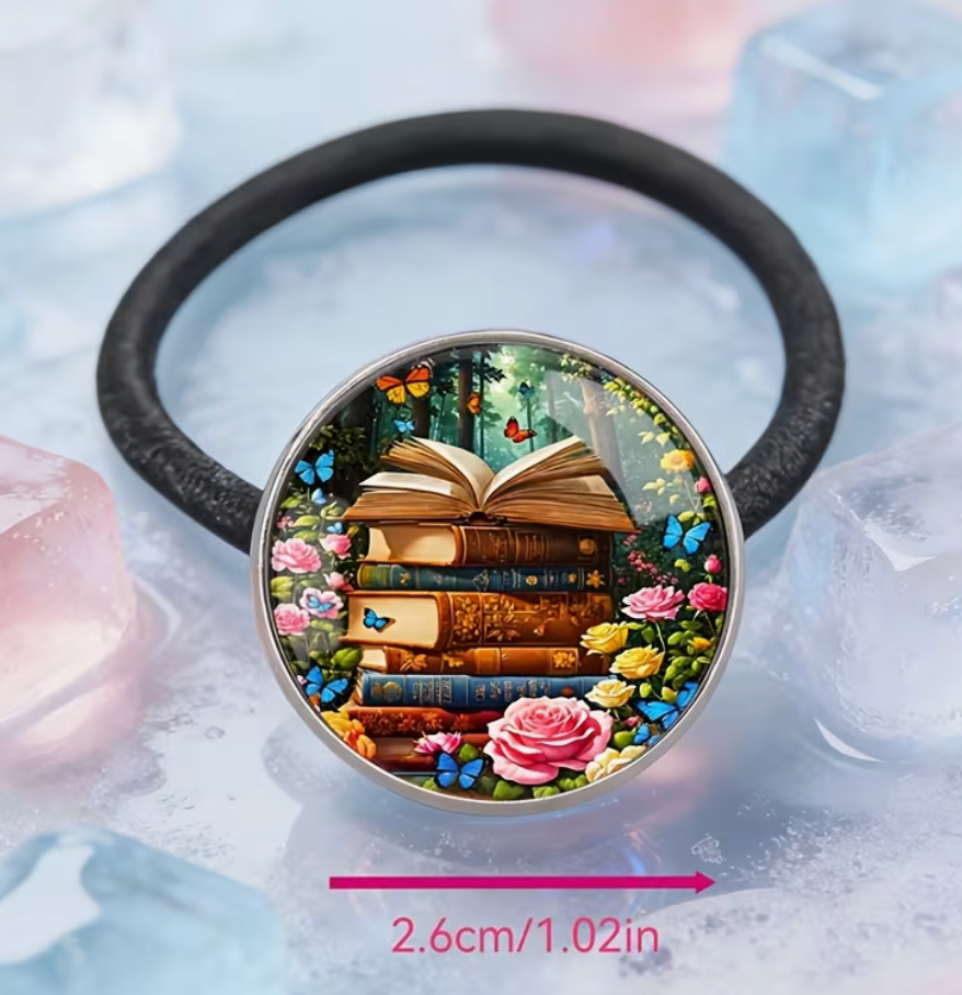 Bookish black hair tie with round centerpiece featuring stacked books, an open book, colorful flowers and butterflies