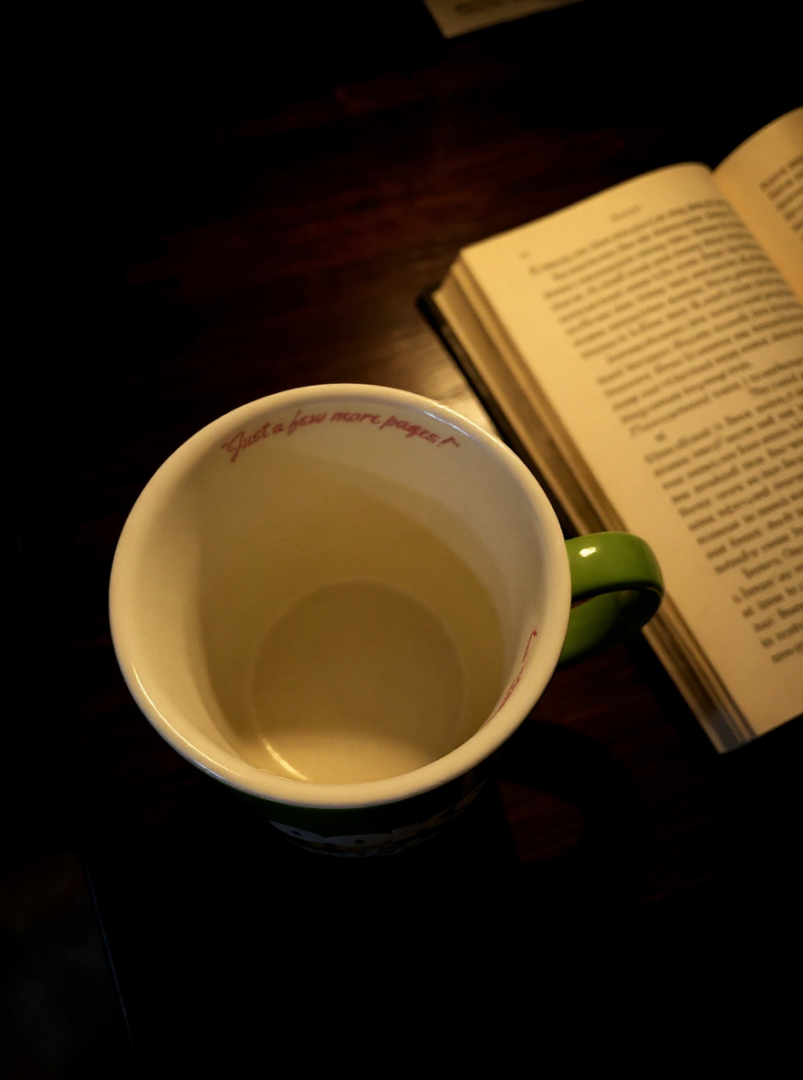 inside of green mug showing Just a few more pages message near rim beside open book