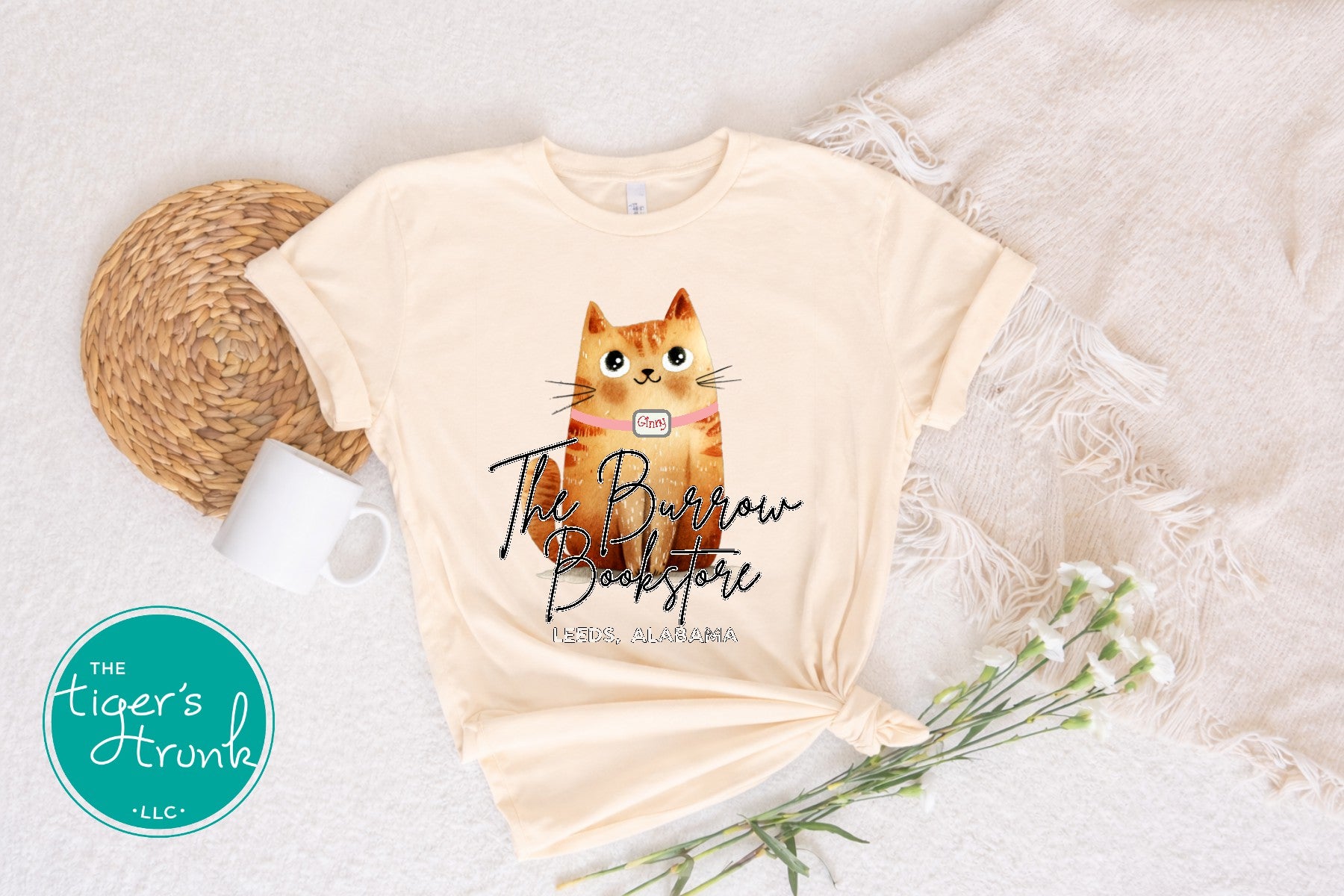 The Burrow Bookstore cat shirt with illustrated orange cat design on a soft cream t-shirt