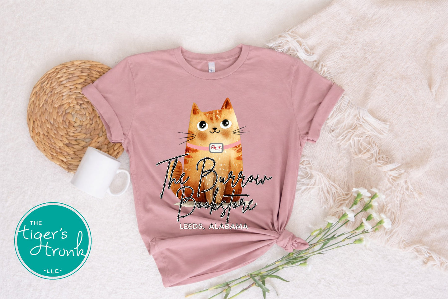 The Burrow Bookstore cat shirt with illustrated orange cat design on a soft mauve t-shirt