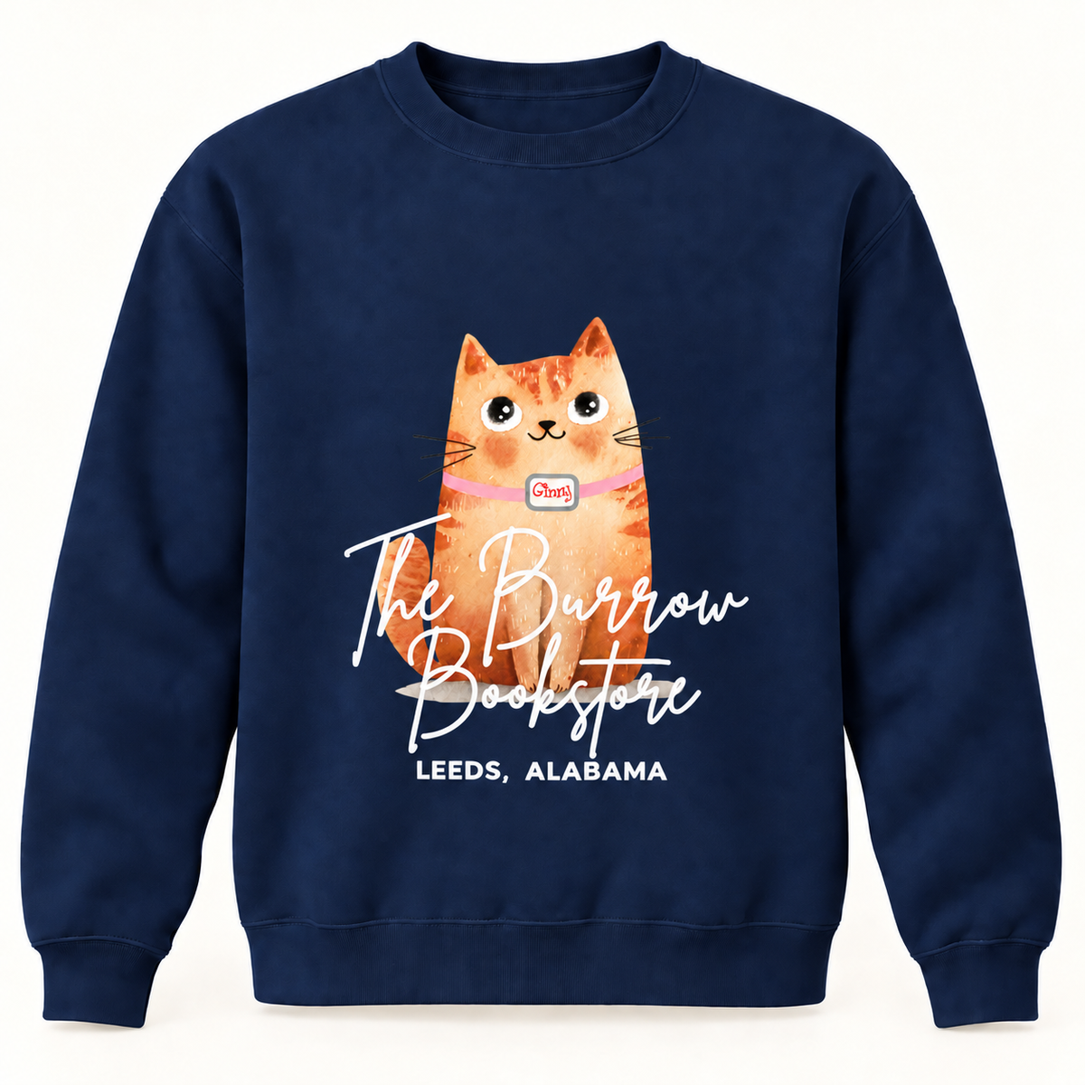 A navy blue crewneck sweatshirt featuring a graphic of an orange tabby cat wearing a pink collar with a small map pin. Below the cat, the text 'The Burrow Bookstore' is written in white script, with 'LEEDS, ALABAMA' underneath.