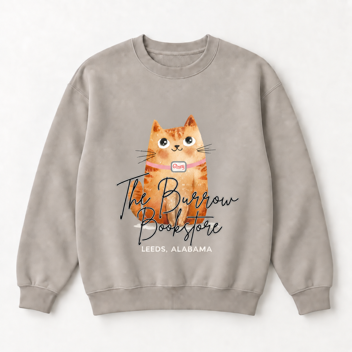 A light taupe crewneck sweatshirt featuring a graphic of an orange tabby cat wearing a pink collar with a book logo, overlaid with the text 'The Burrow Bookstore' and 'LEEDS, ALABAMA'.