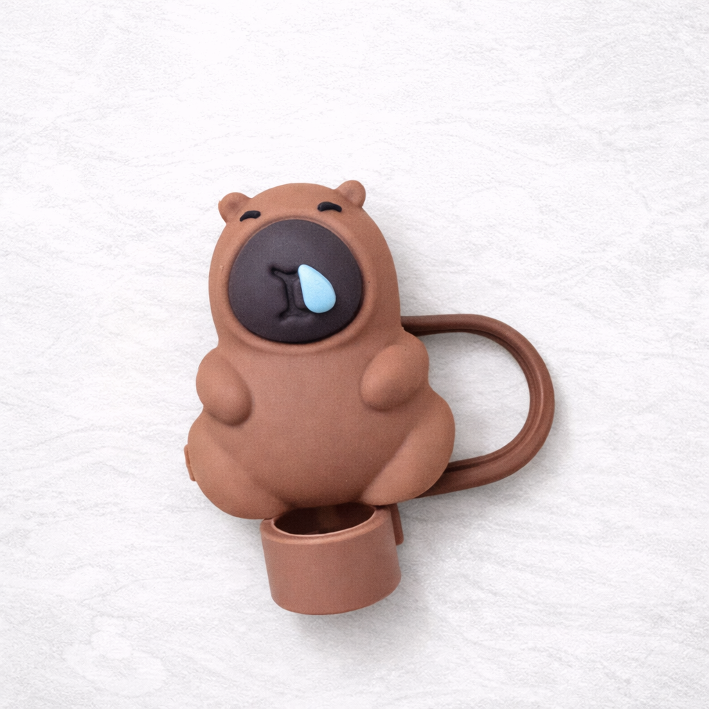 Brown bear-shaped silicone straw topper with a sleepy expression and blue droplet detail, attached to a matching flexible loop for reusable tumbler straw.