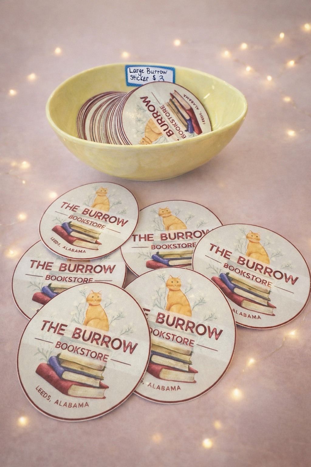 Ginny cat sticker from The Burrow Bookstore in Leeds Alabama displayed with bookstore logo stickers for fundraiser.