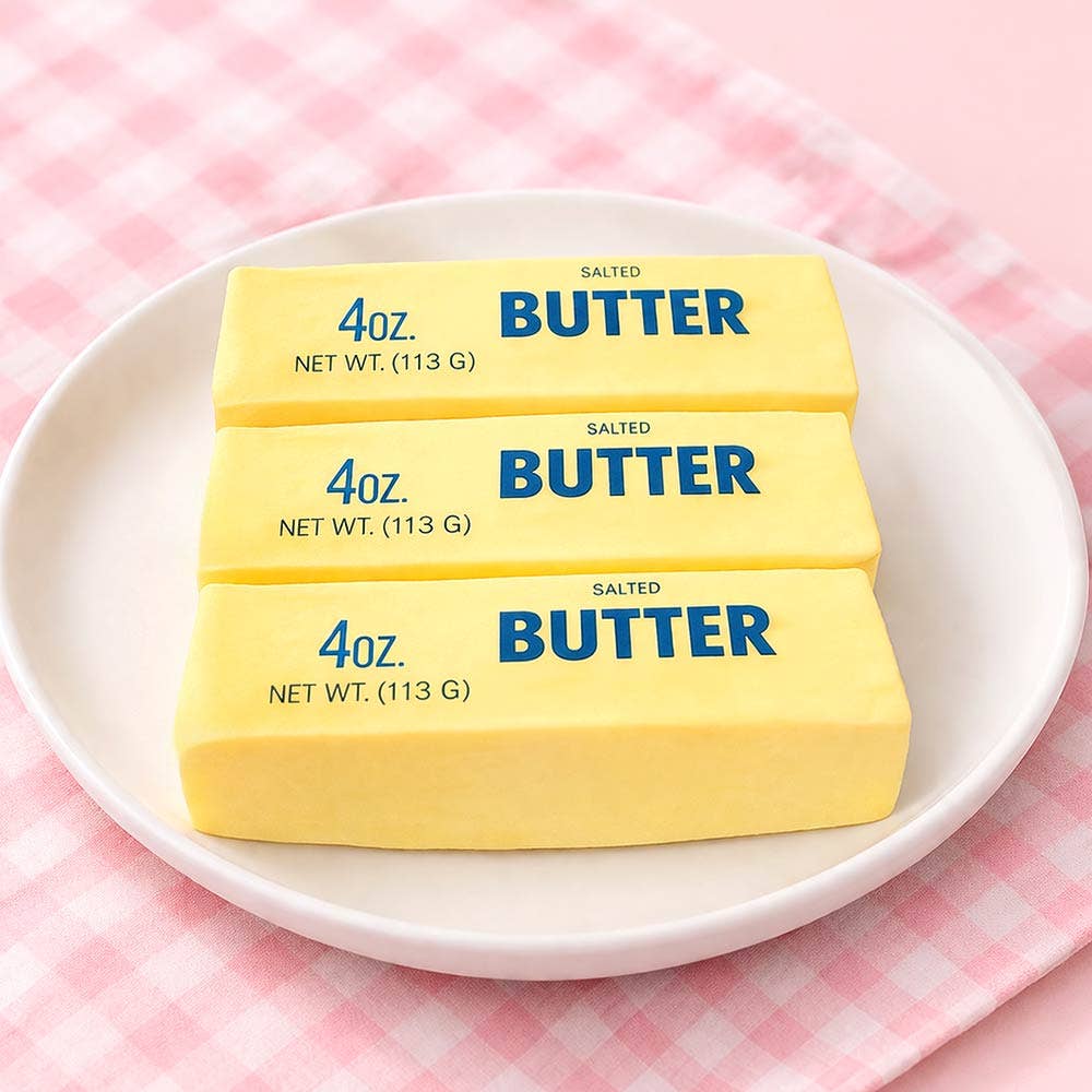 Three butter stick squishy toys on plate with pink background