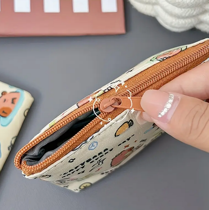 Hand holding a small pouch with a zipper, featuring cartoon animal designs on a gray surface.