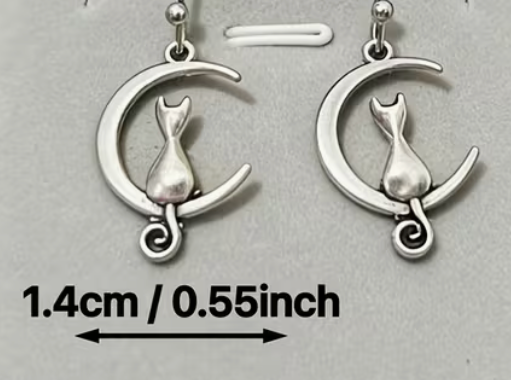 Silver-tone cat and crescent moon dangle earrings with charms measuring approximately .55 inches wide.