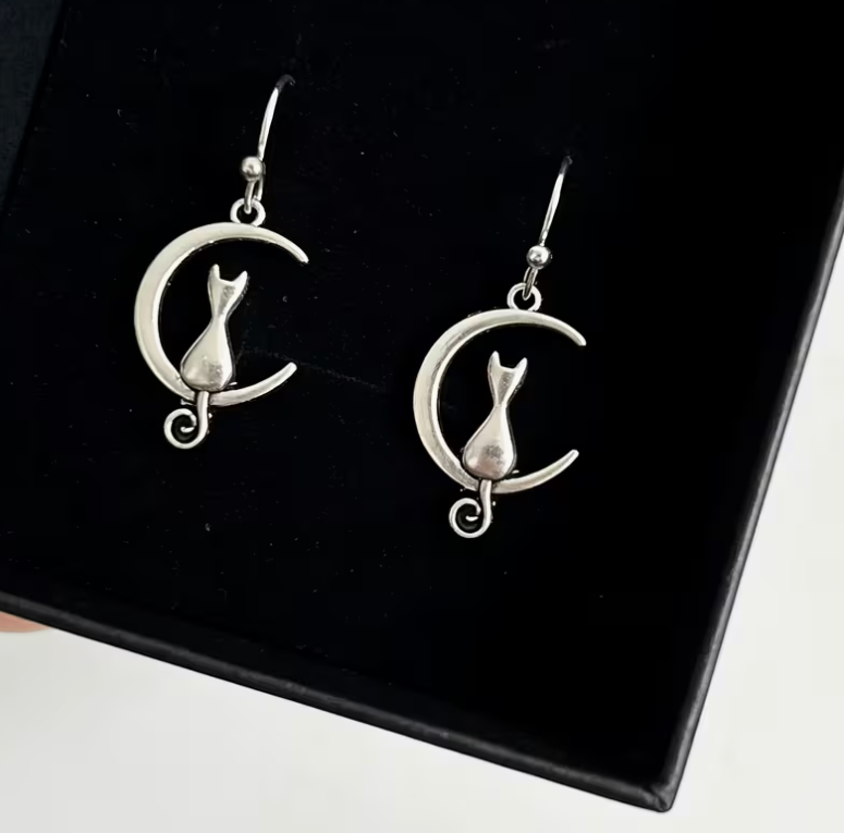 Silver-tone dangle earrings featuring a cat sitting inside a crescent moon with curled tail.