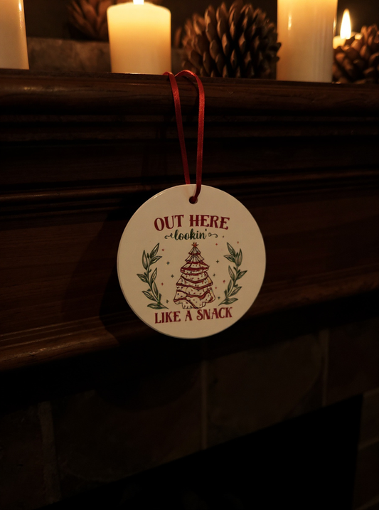 Ceramic ornament with the phrase “Out Here Lookin’ Like a Snack” and a festive illustrated snack hanging by a red ribbon