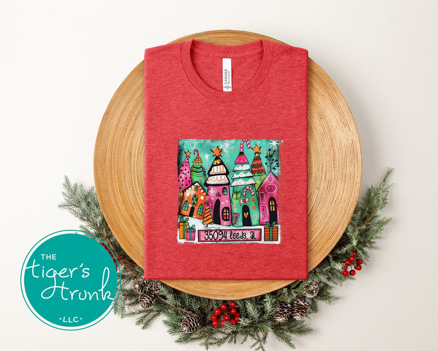 Red t-shirt with a colorful graphic on a wooden plate with decorative elements, featuring 'The Tiger's Trunk' logo.