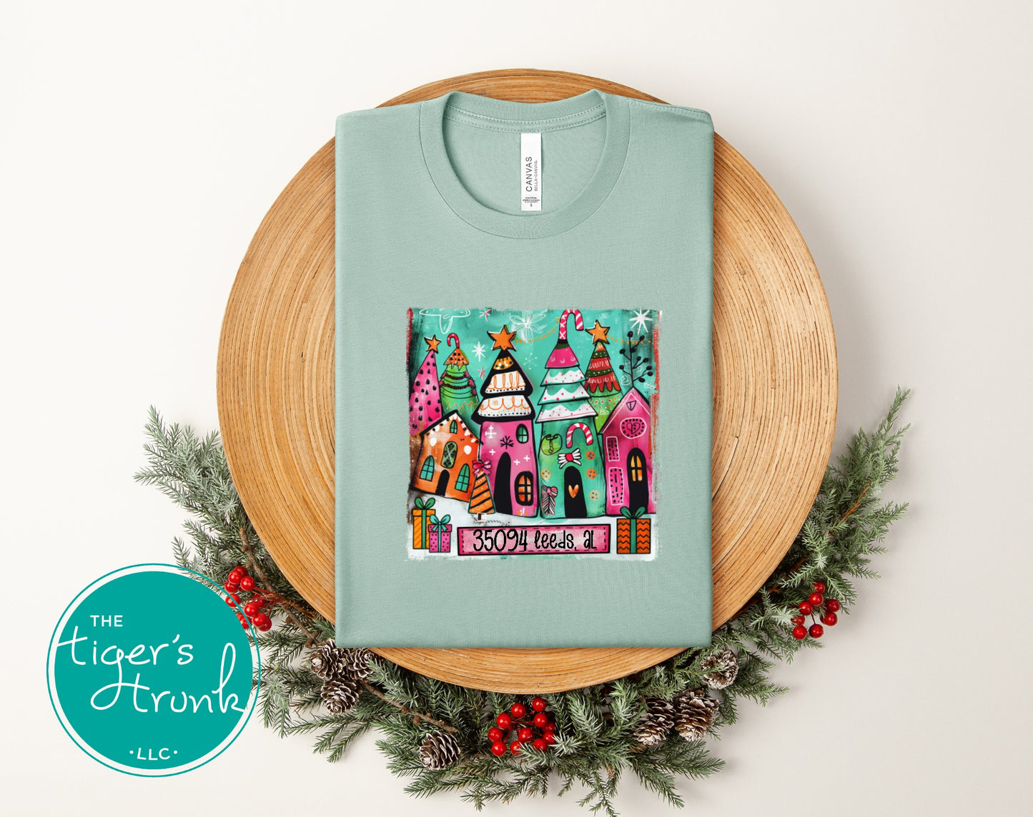 Dusty blue Christmas shirt showing colorful small town holiday houses and 35094 Leeds AL text